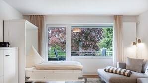 Une chambre moderne dotée d’un lit convertible, d’un canapé, d’une table basse et d’une grande fenêtre donnant sur la verdure.