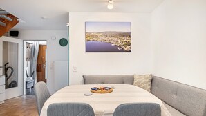 Une pièce moderne comprenant une table à manger, un canapé recouvert d’un tissu gris et un tableau représentant un paysage urbain accroché au mur.