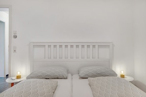 Een tweepersoonsbed met een wit hoofdeinde, twee nachtkastjes met lampen, en beddengoed met een patroon.