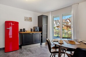 Een compacte keuken met een rode koelkast, een koffiezetapparaat en een eethoek met een tafel en stoelen.