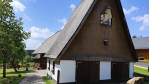 Ein traditioneller Schuppen mit einem steilen Satteldach, einem kleinen Fenster mit Verzierungen und einer Schotterauffahrt zum Eingang.