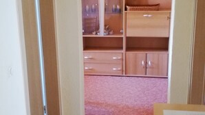 Ein Zimmer mit Fliesenboden, einer Holztür, einem Schrank mit Regalen und einer Kiste auf dem Boden.