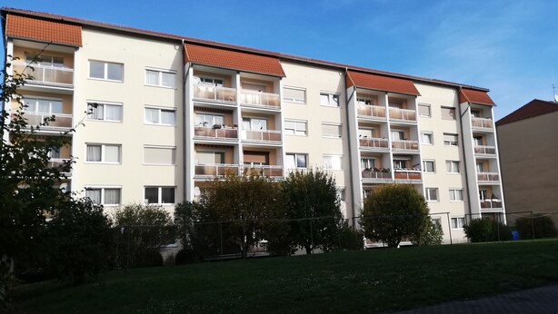Ein mehrgeschossiges Wohngebäude mit Balkonen, einer flachen Dachterrasse und wolkenlosem Himmel.