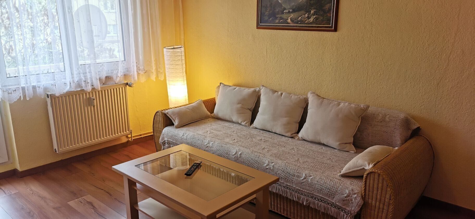 Una sala de estar con un sofá, una mesa de centro de vidrio, un radiador y una ventana con cortinas.