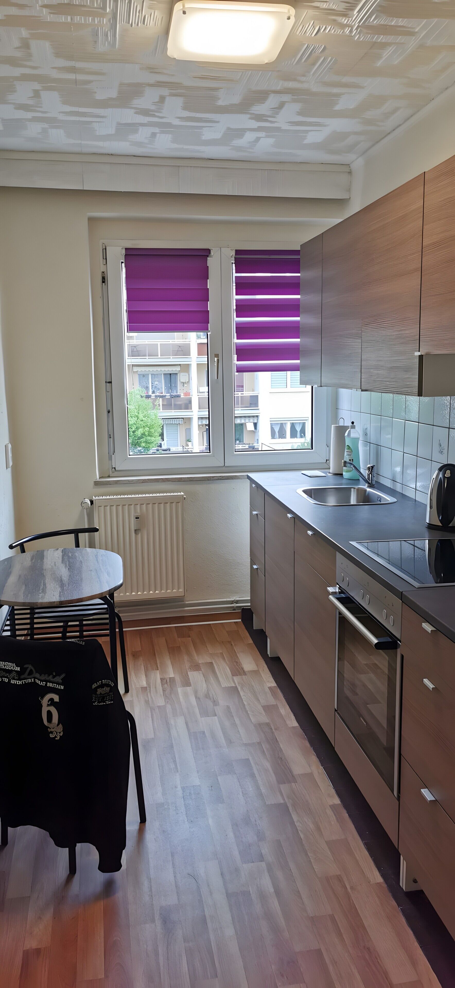 A modern kitchen with a window, wooden cabinets, a built-in oven, and a dining area with a table and chairs.