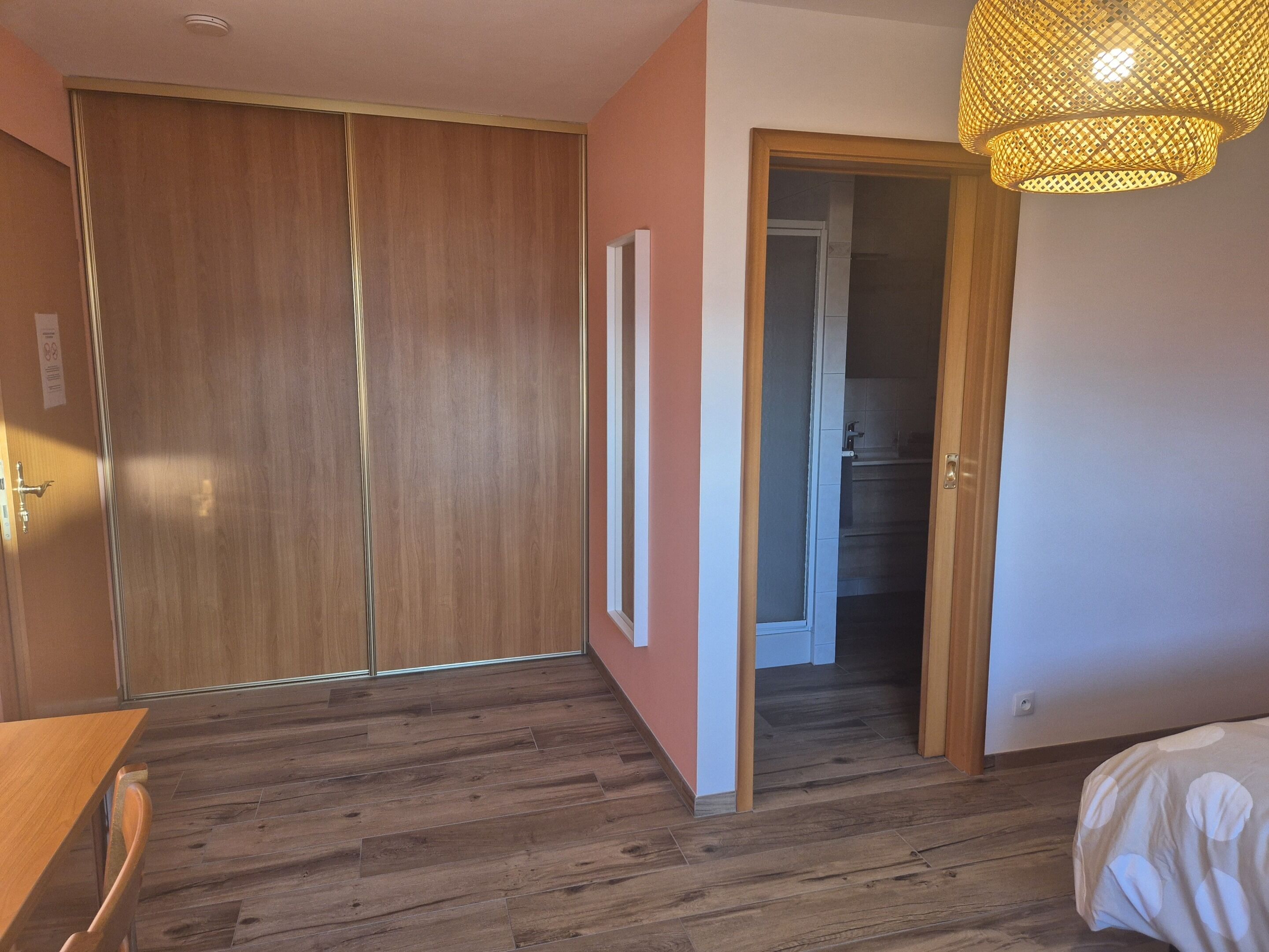 A bedroom with wooden flooring, a bed, a wardrobe, and a door leading to a bathroom.