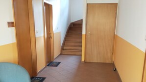 A hallway with a blue chair, wooden doors, a staircase, and a welcome mat. - Chambres Thirion (Saint-Hippolyte)