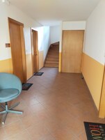Un pasillo con una silla azul, puertas de madera, una escalera y un felpudo.