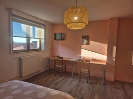 Una habitación con cama, un escritorio y silla, televisor y un ventanal grande.