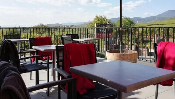 An outdoor patio with tables and chairs, red umbrellas, and a view of the countryside. - Chambres Thirion (Saint-Hippolyte)