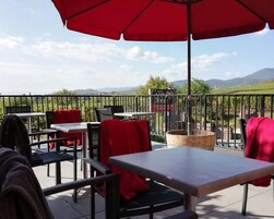 Un patio al aire libre con mesas y sillas, sombrillas rojas y vistas al campo.