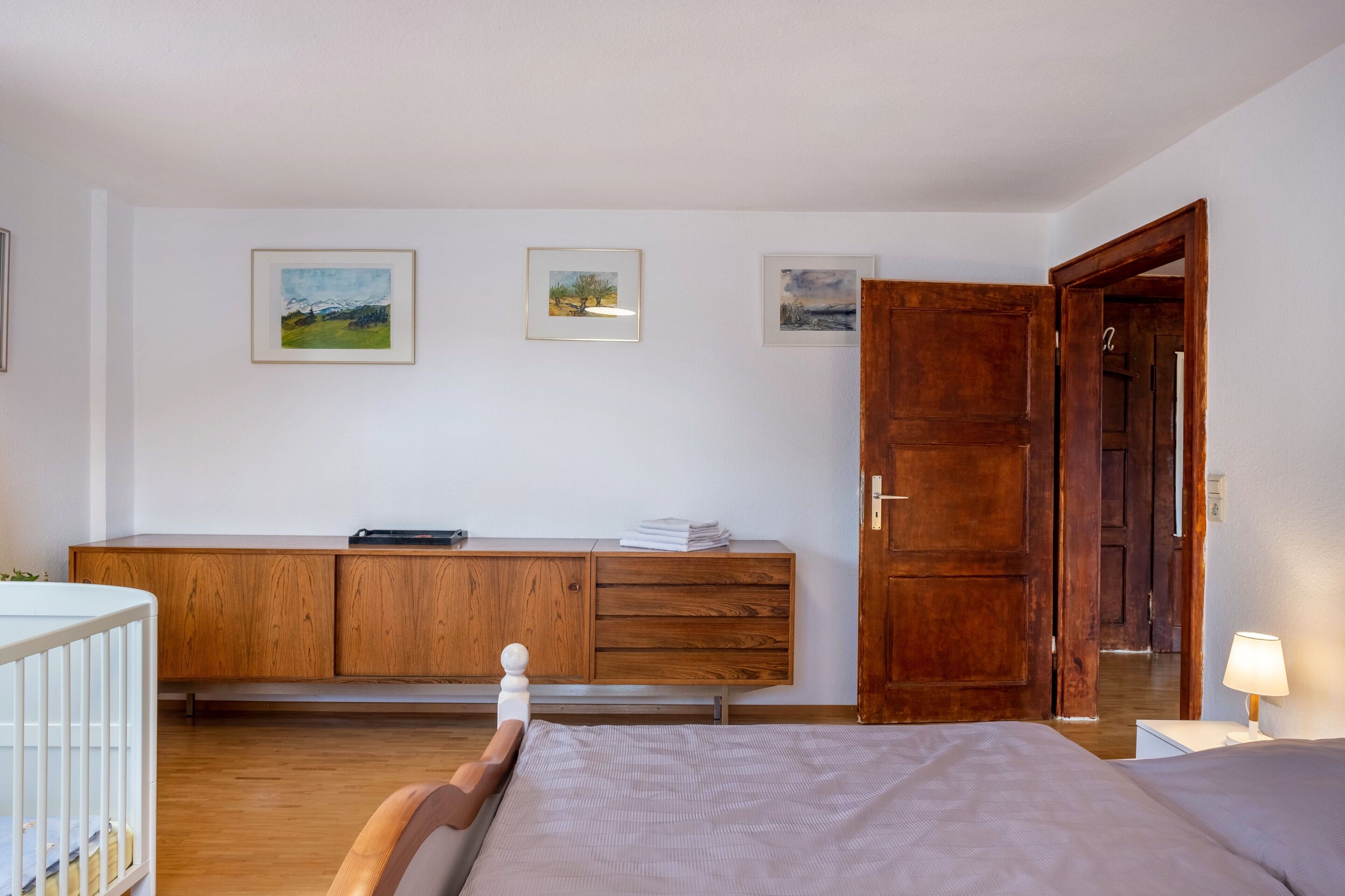 A bedroom with a wooden bed, a nightstand, a wooden dresser, and a door leading to another room.