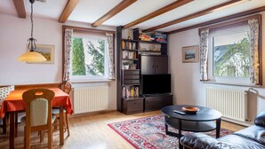 A living room with a dining table, a sofa, a TV, a bookshelf, and large windows. - Apartment '85qm, 2 Schlafzimmer' with Mountain View, Private Terrace and Wi-Fi (St. Märgen)