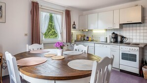 A kitchen with white cabinets, a wooden dining table with placemats, and a window with curtains. - Apartment '85qm, 2 Schlafzimmer' with Mountain View, Private Terrace and Wi-Fi (St. Märgen)