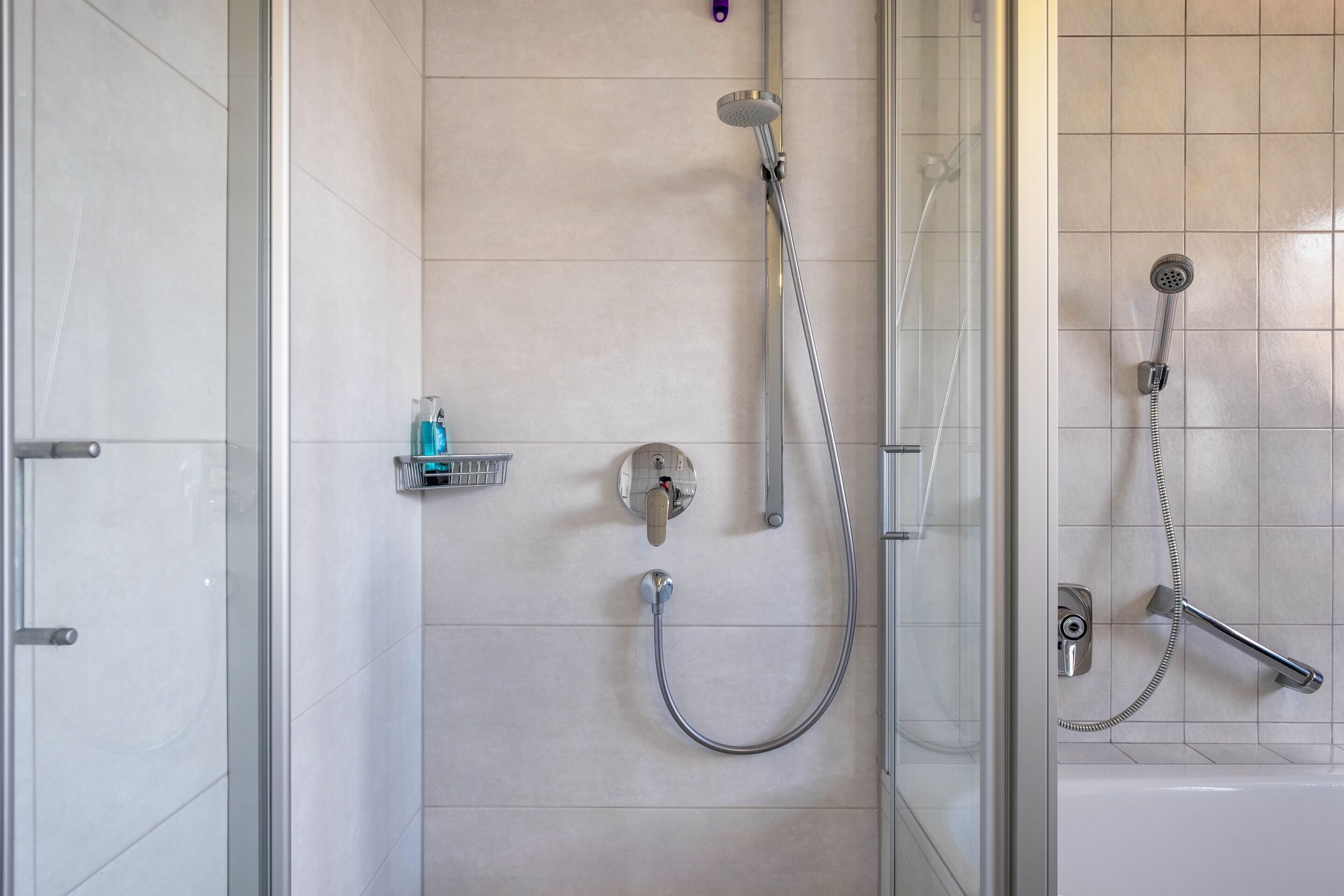 Ein modernes Badezimmer mit Duschkabine aus Glas, Handbrause, Wandarmatur und einer kleinen Ablage für Toilettenartikel.
