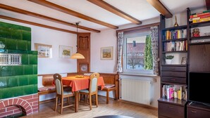 A cozy room with a green cushioned bench, wooden dining table, and chairs. There's a bookshelf with books and a television on a stand. - Apartment '85qm, 2 Schlafzimmer' with Mountain View, Private Terrace and Wi-Fi (St. Märgen)