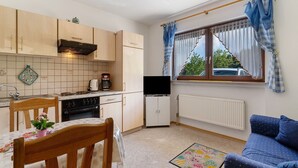 Cocina compacta con comedor, televisor y ventana con cortinas.