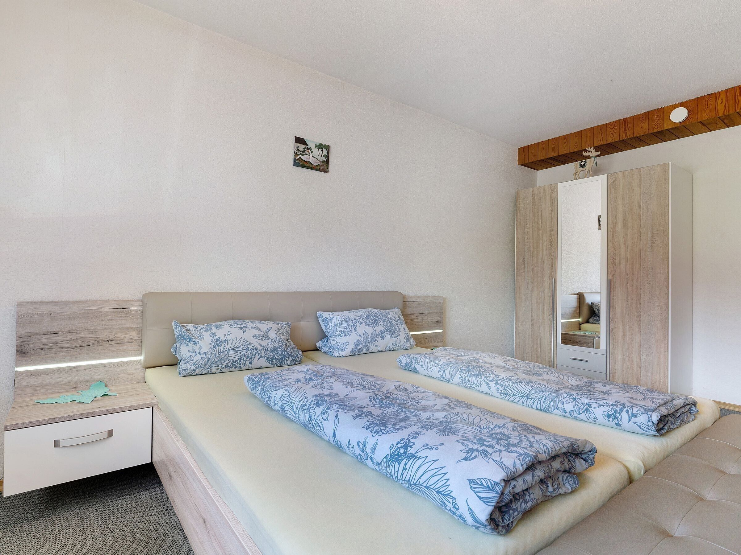 Ein Doppelbett mit Blumenmuster, ein Nachttisch mit Lampe, ein Kleiderschrank und ein kleines Bild an der Wand.