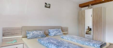 Ein Doppelbett mit Blumenmuster, ein Nachttisch mit Lampe, ein Kleiderschrank und ein kleines Bild an der Wand.
