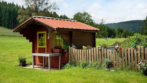 Una cabaña de madera con techo rojo, valla de madera y una mesa afuera.