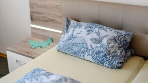 Una cama con un cojín estampado de flores, una mesita de noche de madera y un adorno azul aguamarina.