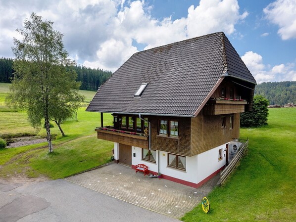 Ein zweistöckiges Holzhaus mit geneigtem Dach, einem Balkon und einer gepflasterten Auffahrt.