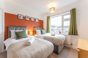 Quarto de hotel com duas camas, janela com cortinas, radiador e quadros nas paredes.