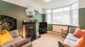 A living room with a fireplace, sofa, and a TV displaying 'NETFLIX'. - Host Stay The Headlands (Coventry)