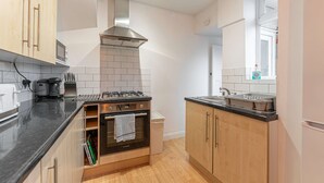 A modern kitchen with wooden cabinets, a gas stove, a stainless steel range hood, and a window providing natural light. - Host Stay The Headlands (Coventry)