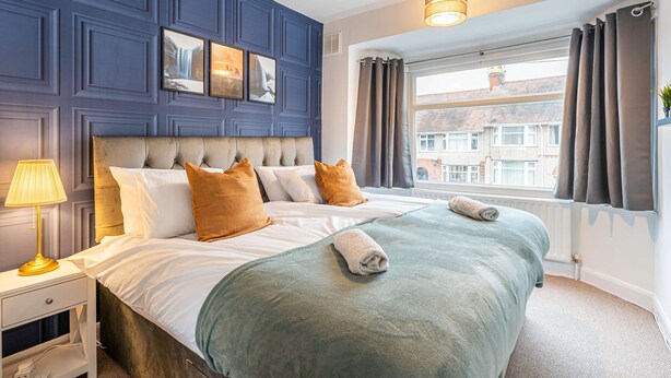 A neatly made bed with a green blanket, a headboard, and two pillows. - Host Stay The Headlands (Coventry)
