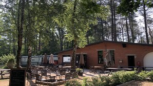 An outdoor patio area with tables and chairs, surrounded by trees and a brick building. - Cozy Chalet with Terrace (Wechelderzande (Lille))