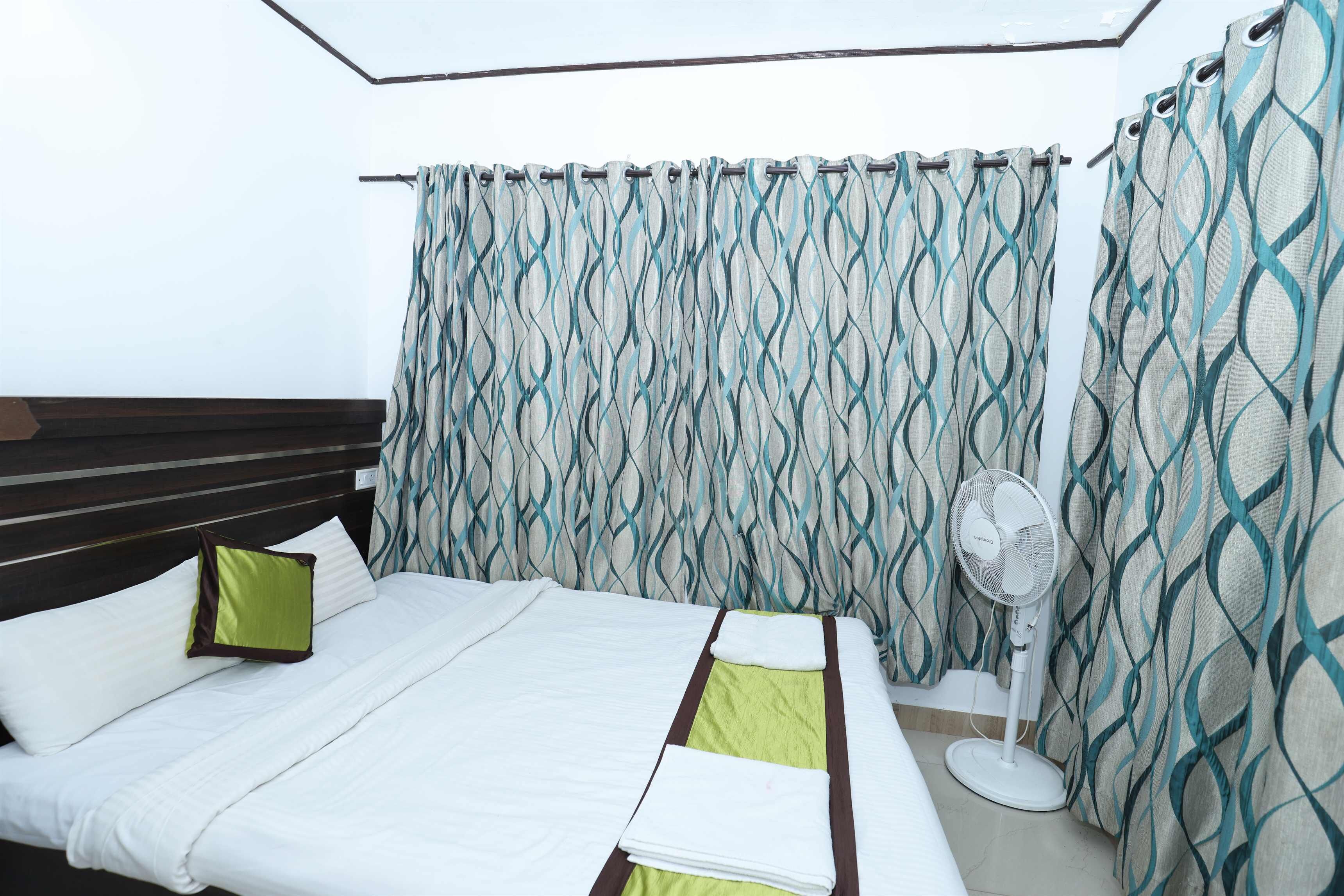A neatly made bed with a green pillow, a white blanket, and a brown bedspread.