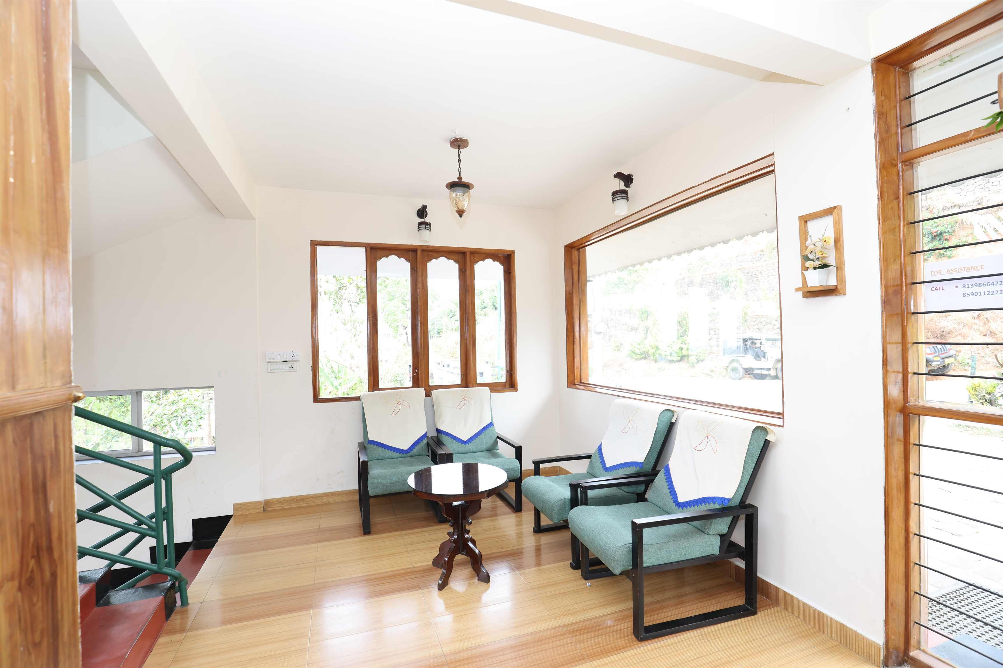 Une pièce dotée d’un plancher en bois, d’une table centrale et de quatre chaises avec des coussins bleus et blancs. De grandes fenêtres à cadre en bois offrent une vue sur l’extérieur.