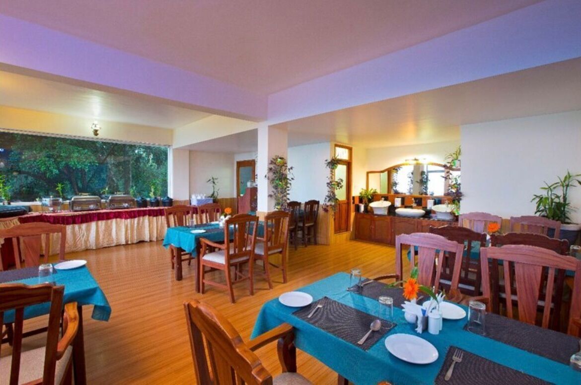 A spacious dining area with multiple tables and chairs, a large window with a view of trees, and a well-lit interior.