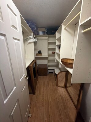Un vestidor estrecho con piso de madera, estantes blancos y un taburete pequeño.