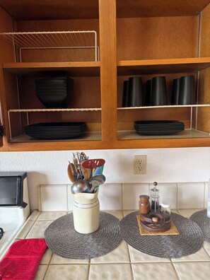A kitchen with wooden shelves, a spice rack, and a countertop with a red cushion.