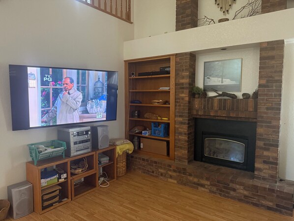 Una sala de estar con televisión de pantalla plana, estanterías de madera, chimenea y pared de ladrillo.