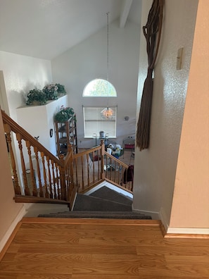 A wooden staircase leading to a living area with a dining table, chairs, and a hanging light fixture.