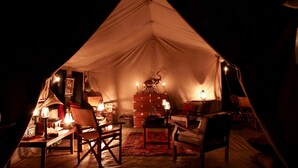 A cozy tent interior with a dining table, chairs, a lamp, and a decorative animal head. - Sentinel Mara Camp (Maasai Mara)
