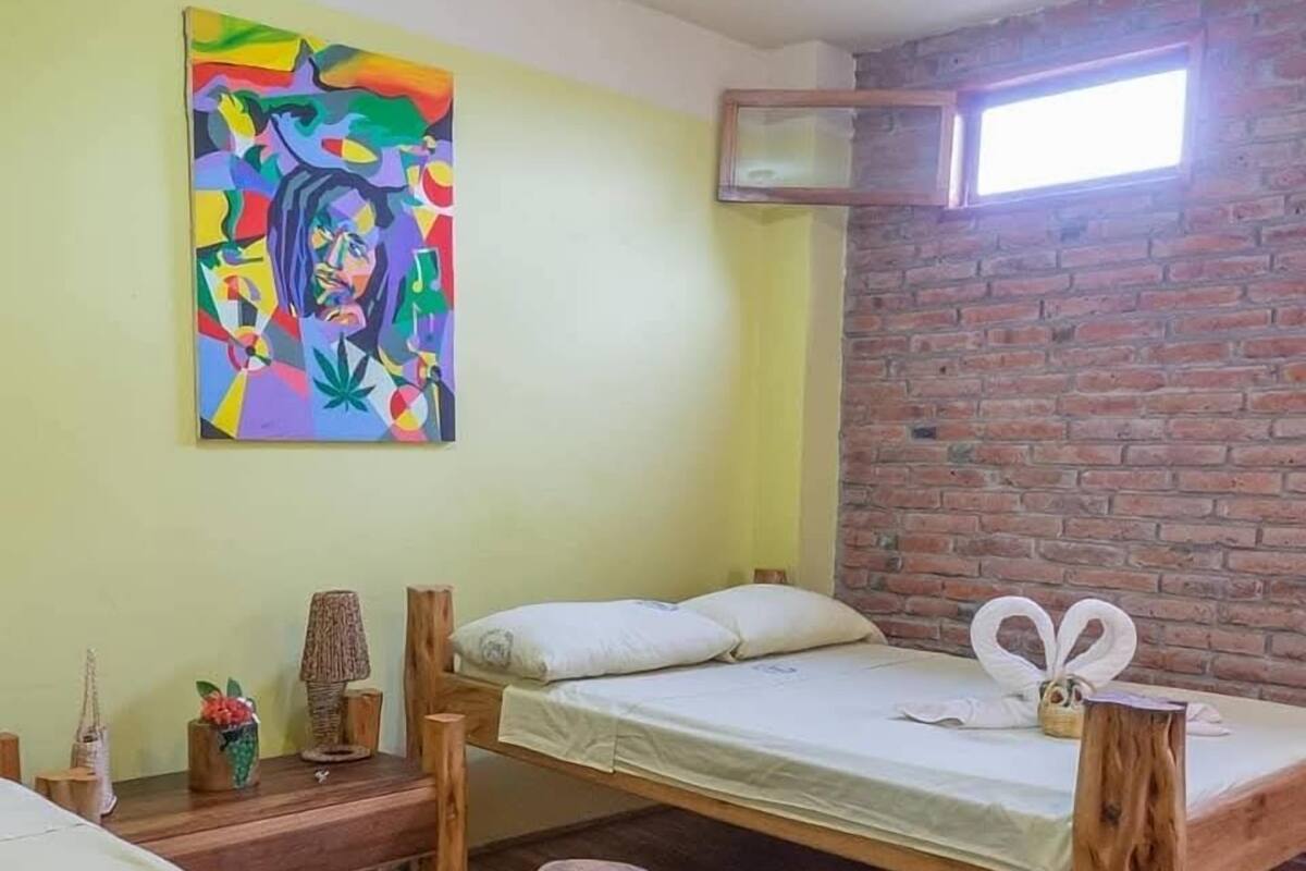 Una habitación con literas, un cuadro abstracto de colores, una pared de ladrillo y una ventana.