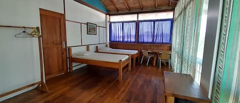 Quarto com duas camas de solteiro, uma mesa de madeira, uma cadeira e uma janela com cortinas.