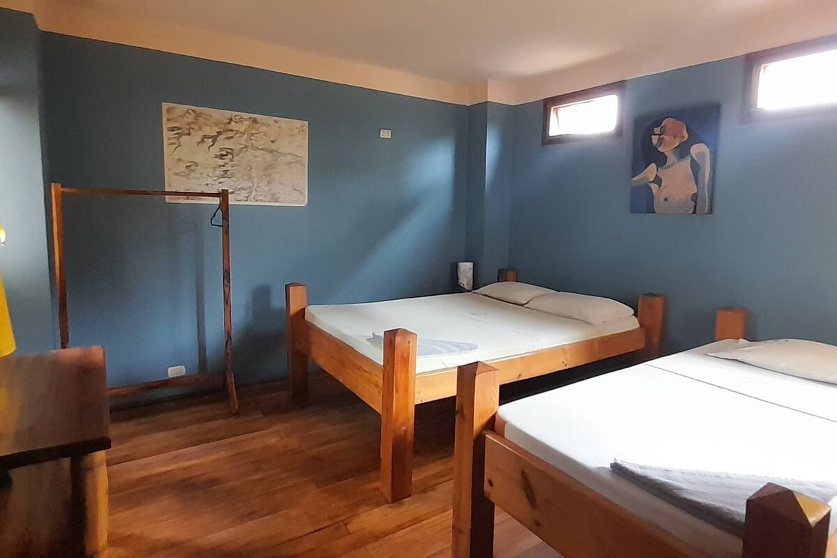 Una habitación con dos camas de madera, una silla de madera, un mapa en la pared y una ventana.
