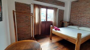 A room with a wooden bed, a wooden chair, a wooden table, and a brick wall.