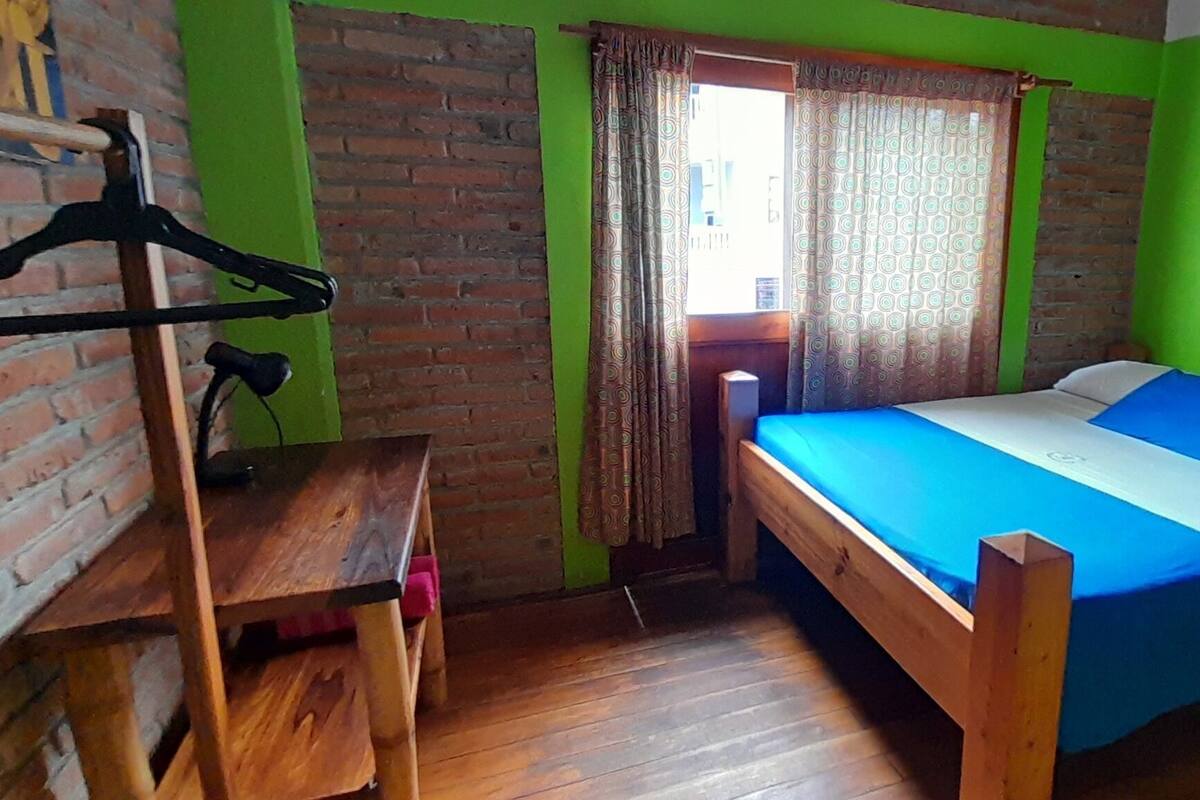 Una habitación con una cama, un escritorio de madera, un perchero y una pared de ladrillo.
