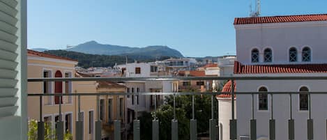 Un balcó amb caires blanques i una taula petita, amb vista a un paisatge urbà amb edificis i una muntanya a la distància.
