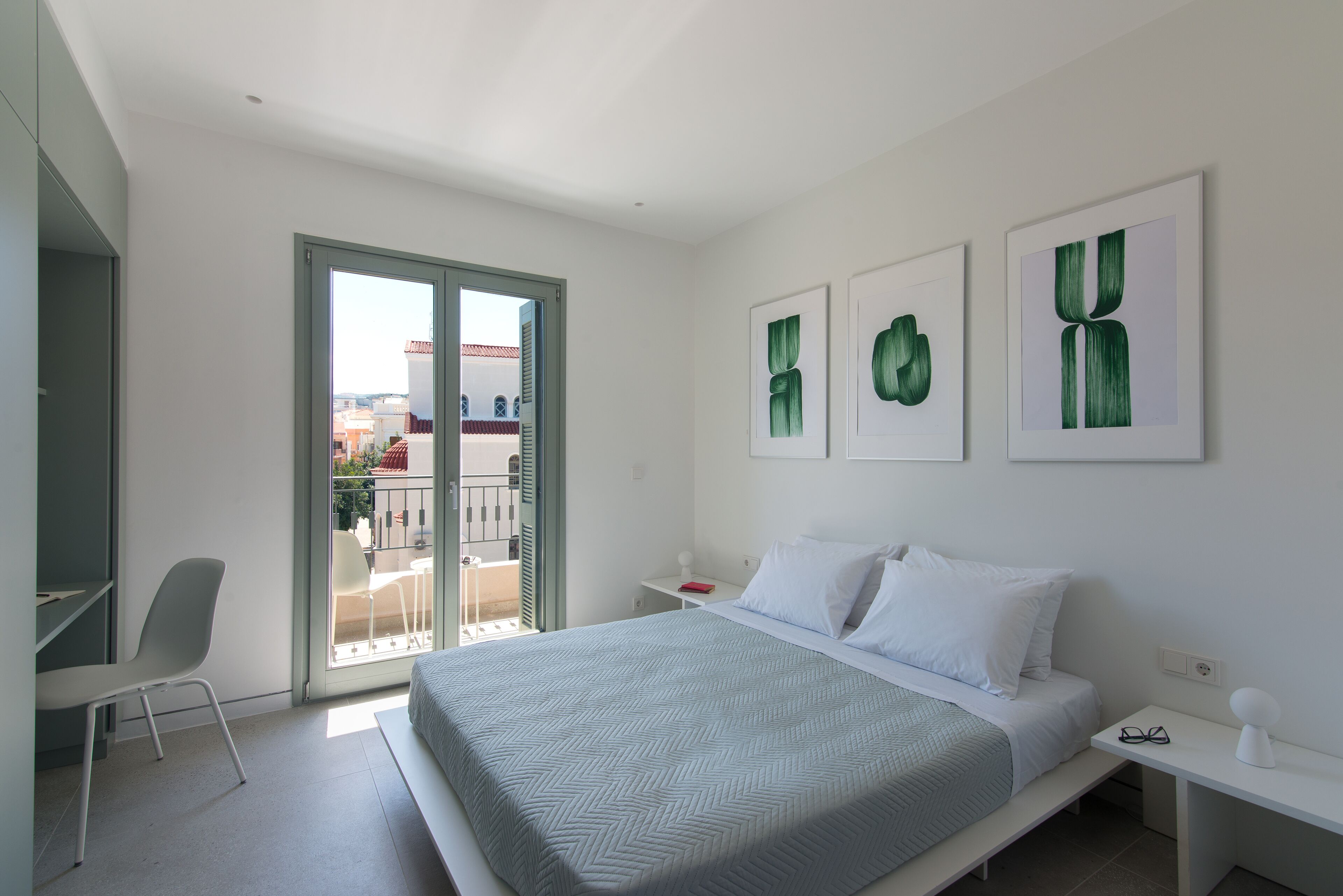 A modern bedroom with a bed, a desk, and a chair. There are three framed artworks on the wall.
