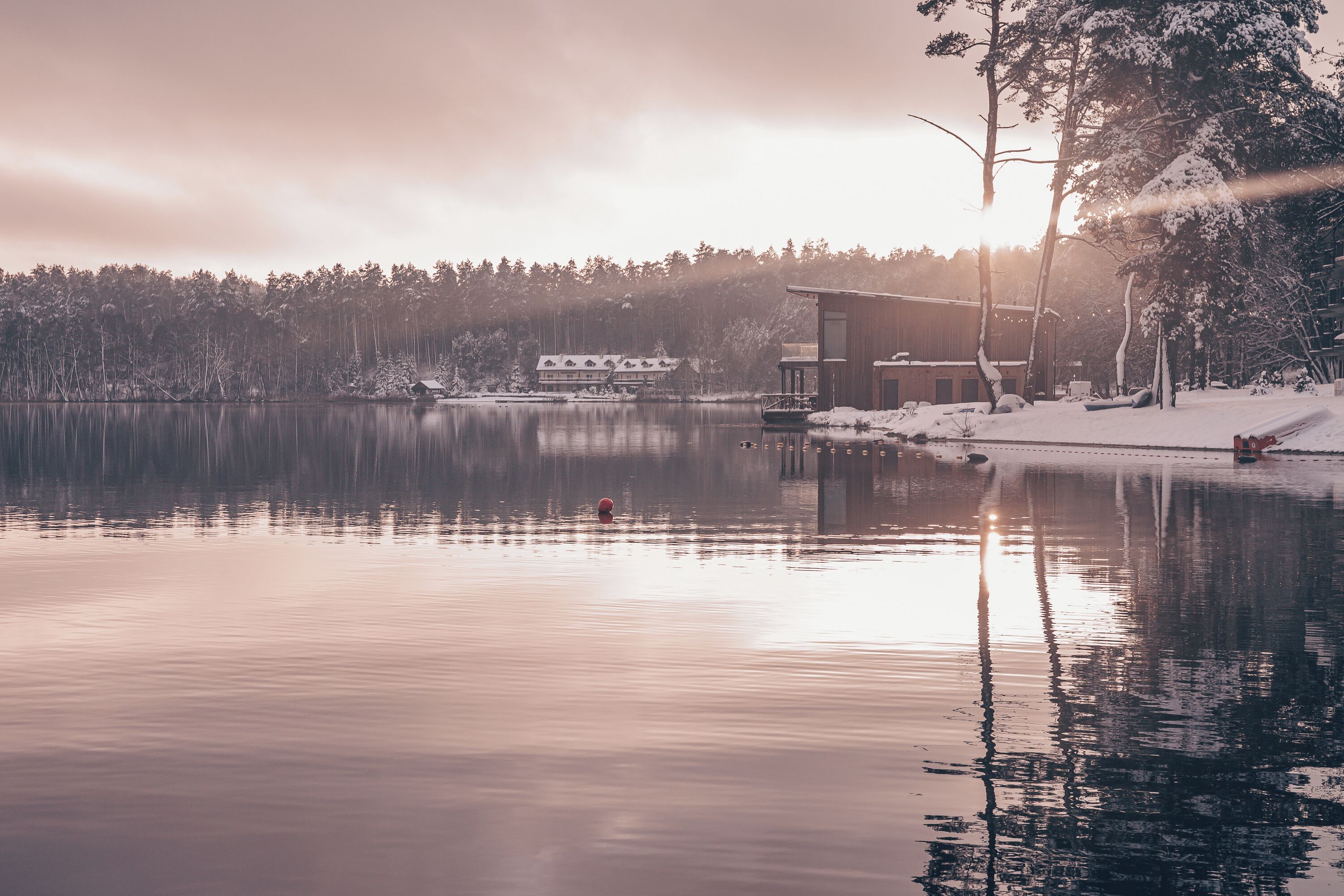 Una propiedad tranquila junto al lago con una cabaña moderna, un muelle y un paisaje cubierto de nieve.