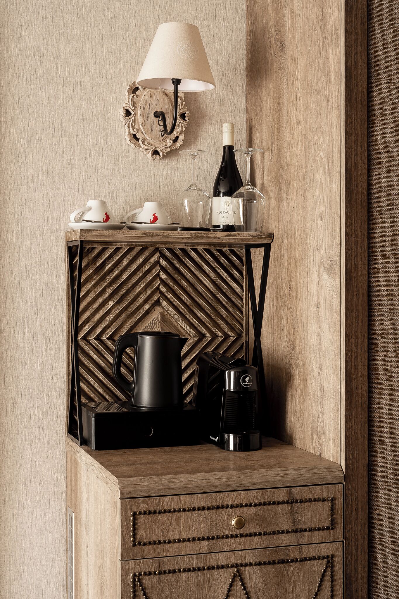 Un comodino in legno con una lampada, una bottiglia di vino, bicchieri e una macchina per il caffè.