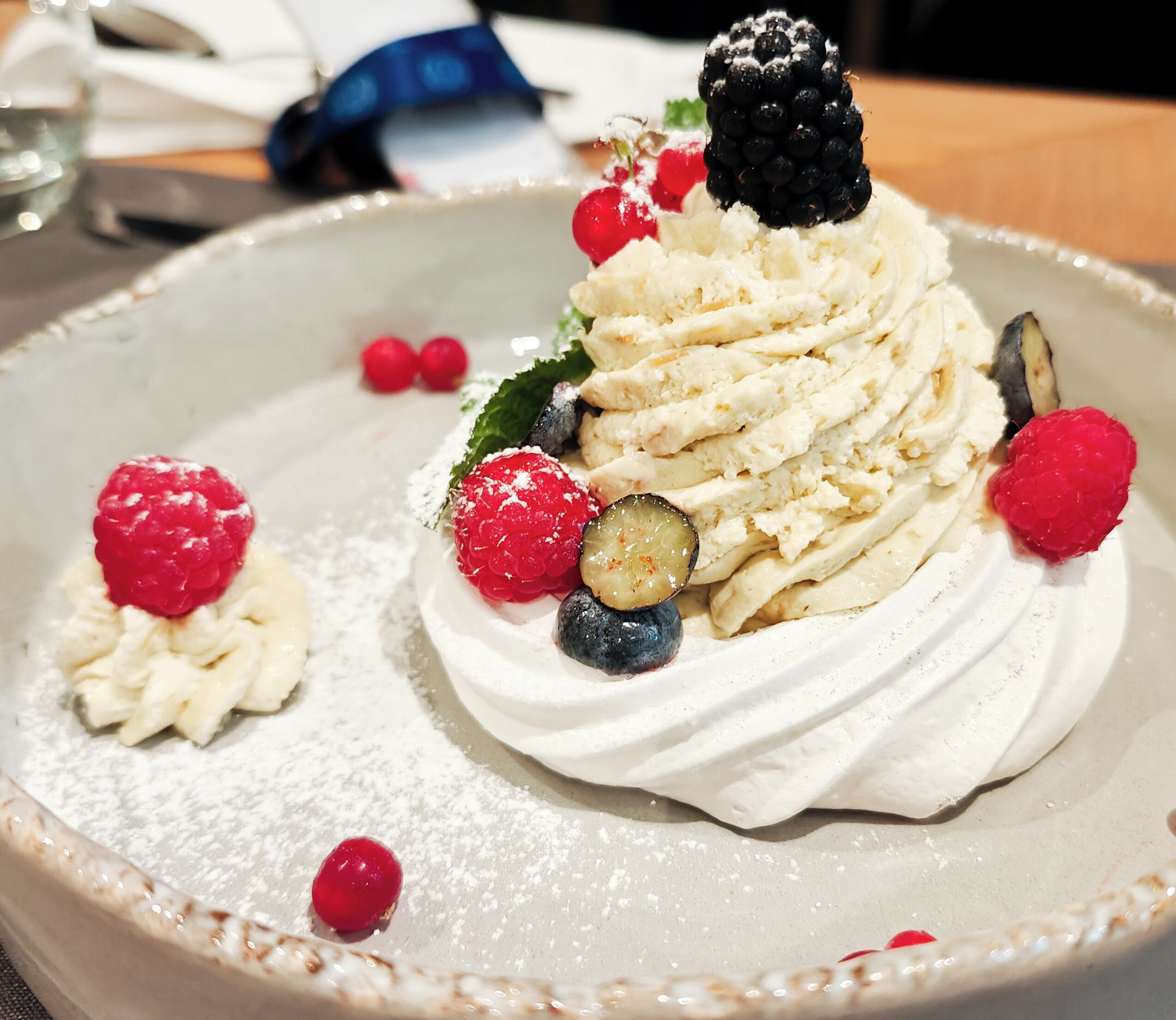 Postre amb nata, baies i una grosella sobre un plat.