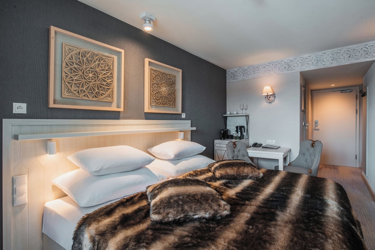 Habitación de hotel moderna con una cama grande, dos obras de arte enmarcadas, un escritorio con silla y una mesita con espejo y objetos decorativos.